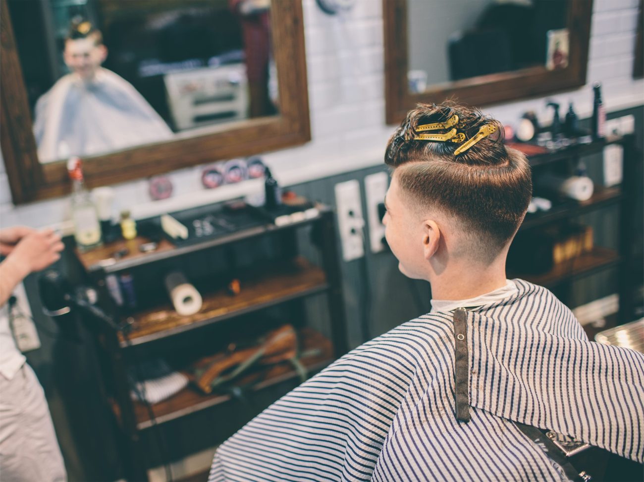 hairstylist and plesed man client with haircut looking in mirror - Diario a pie de barrio Barber trims a client's hair in a vintage-style shop, mirrors and tools visible in the background.