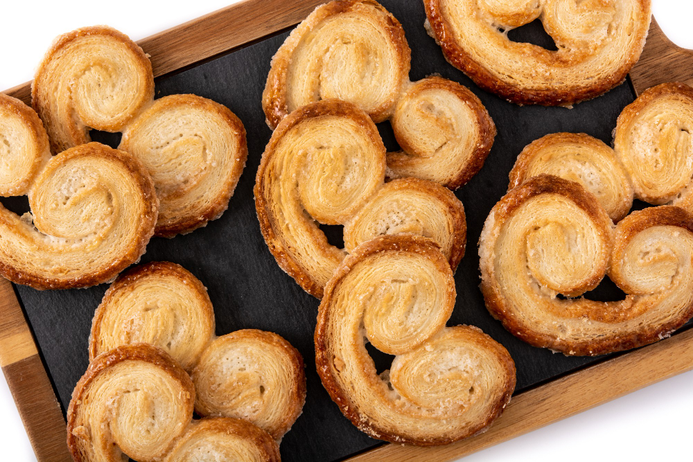 Golden-brown palmier pastries arranged on a wooden board with a dark slate tray