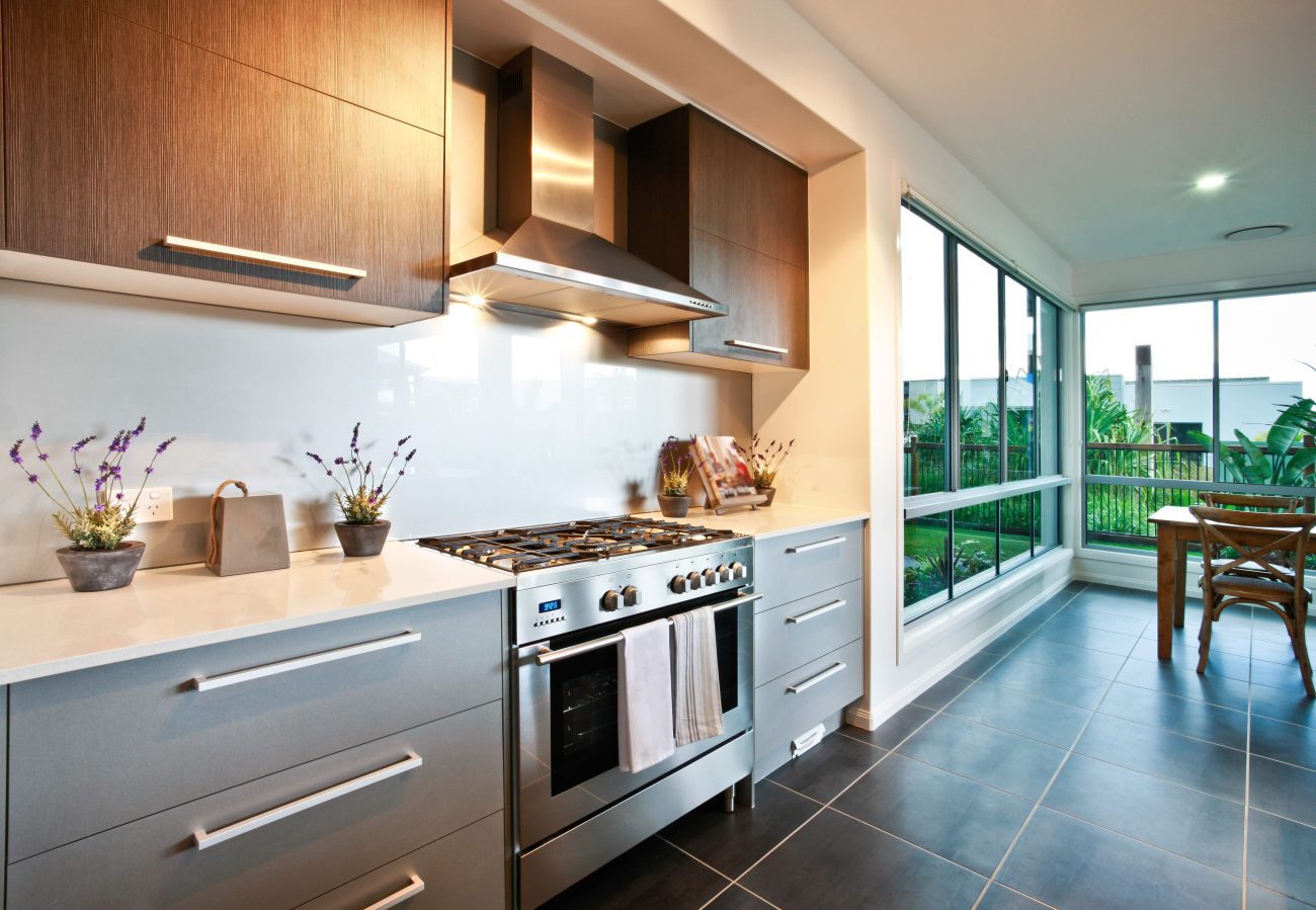777554 - Carpintería Molas - Diario a pie de barrio Modern kitchen with a stainless steel gas range and hood, gray cabinets, and a white countertop, adjacent to a dining table by large windows.