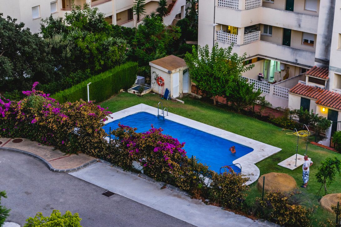 architecture Apartment in Marbella in Spain - Diario a pie de barrio Rectangular blue pool in a residential courtyard, framed by purple flowering hedges and apartment buildings.