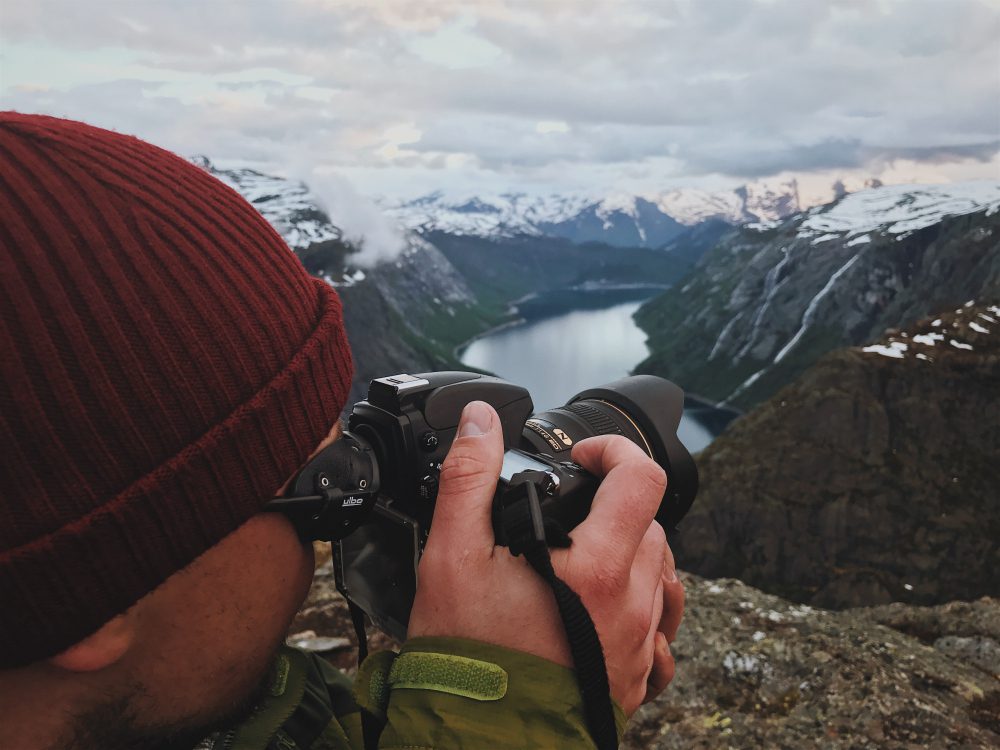 Person in a red beanie taking a landscape photo with a DSLR over a rocky overlook.