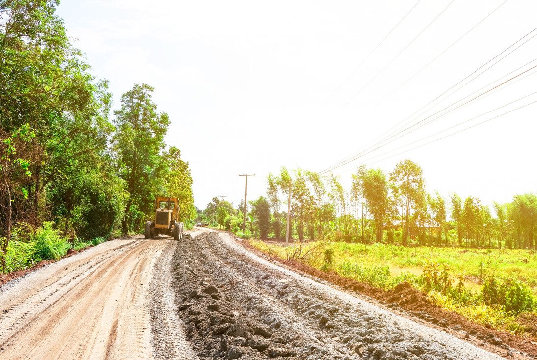 Road Construction and repair Making rural roads - Diario a pie de barrio Rural road under construction with a bulldozer on the left and trees lining the roadside under a sunny sky.